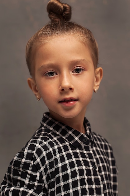 Close-up portrait of a small beautiful girl with blonde hair pulled up in a bun. The child plays and poses. Children's games.