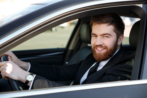 Close up portrait of a smiling bearded man in suit driving car