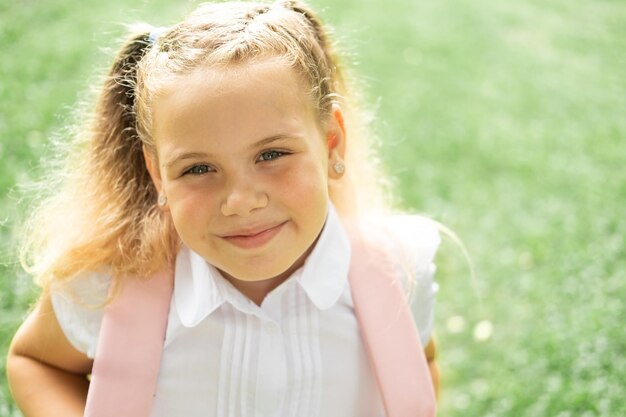 close up portrait of smiling blonde schoolgirl in white shirt with pink backpack back to school outd