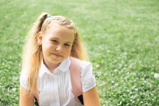 close up portrait of smiling blonde schoolgirl in white shirt with pink backpack back to school