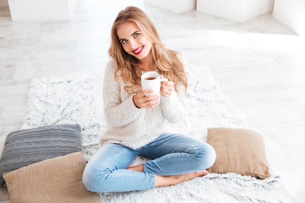 Close up portrait of a smiling happy girl in sweater holding tea cup indoors