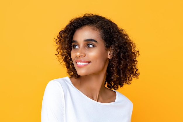 Close-up portrait of smiling young beautiful African American woman thinking while happily looking at the side in isolated studio yellow background