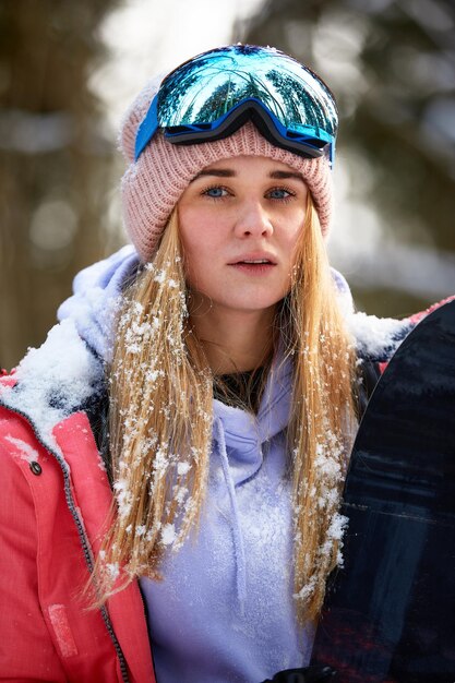 Close up portrait of snowboarder woman at ski resort wearing helmet and goggles with reflection of forest in mountains Free copy space for your information