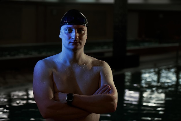 Close up portrait of sporty muscular man in swimming goggles and cap with a naked torso on background of swimming pool indoors