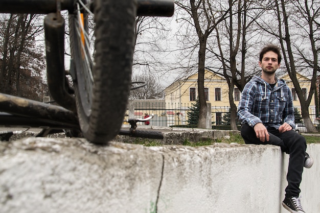 Close up portrait of stylish handsome hipster guy sitting at city park near his bike