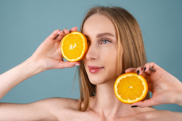 Close-up portrait of topless woman with perfect skin and natural make-up, full nude lips, holding fresh citrus vitamin C orange