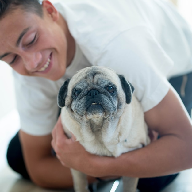 Close up and portrait of two best friends at home together - teenager looking with love at his pug - pet and domestic dog concept