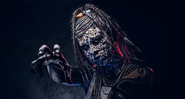 Close-up portrait of a witch from the indigenous African tribe, wearing traditional costume. Make-up concept. Isolated on a dark background.