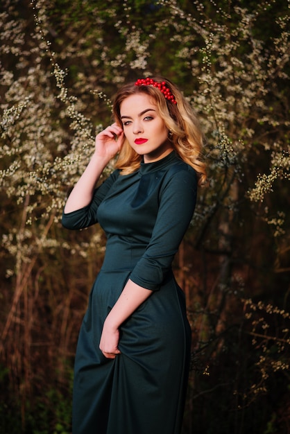 Close up portrait of yong elegant blonde girl at green dress on the garden in spring on blossom trees.