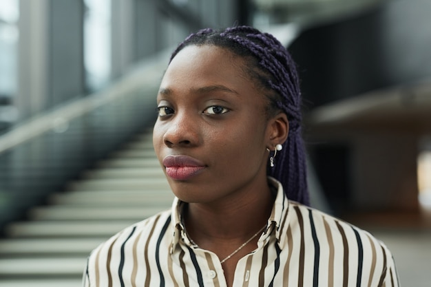 Close up portrait of young African-American businesswoman looking at camera while posing in office hall, copy space