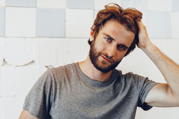 Close up Portrait of a young bearded man standing against grunge weathered wall