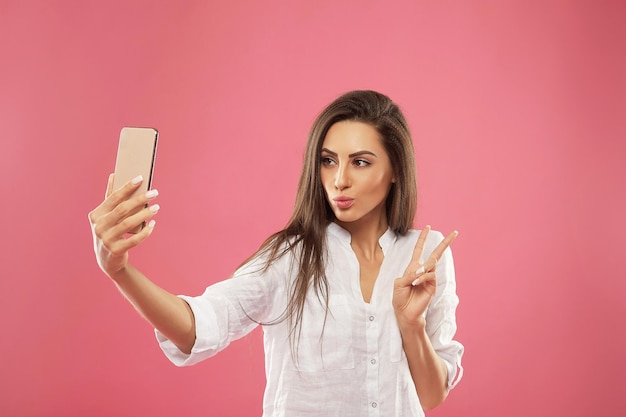 Close up portrait of young beautiful stylish woman making selfie using her own smartphone smiles