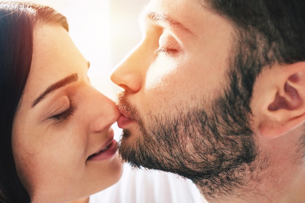 Close up portrait of young beautiful tender couple in love while them are sitting on bed and kissing, hugging and relaxing together. Love, relationships, family and St. Valentines day