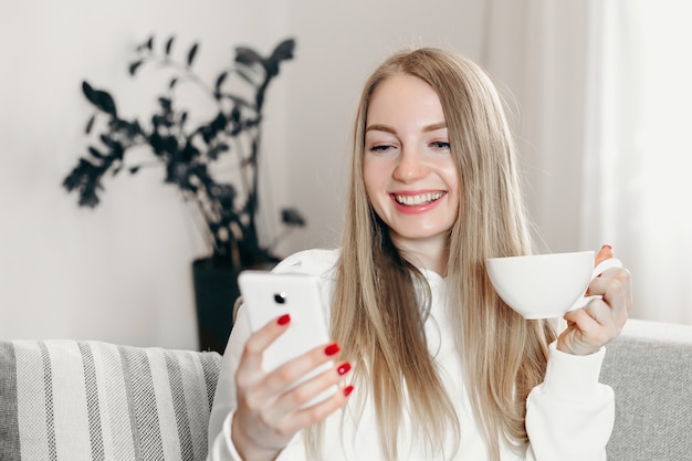 Close up portrait of young blonde female student video calling by phone while quarantined at home