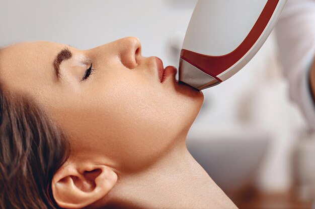 Close-up portrait of a young girl undergoing a non-surgical rejuvenation procedure. Hardware massage for face lifting. Lead the device in the face. The protection from the aging.