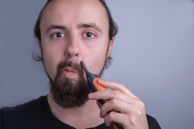 Close-up portrait of a young guy using a mustache trimmer. Beard and mustache care.