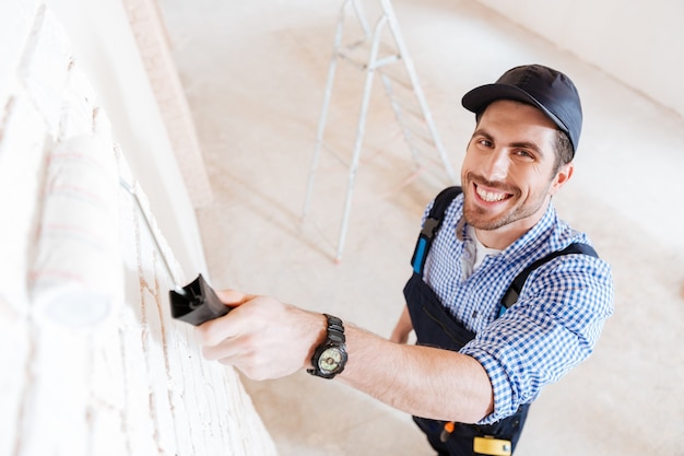 Close-up portrait of a young handsome builder using paint roller in his work indoors