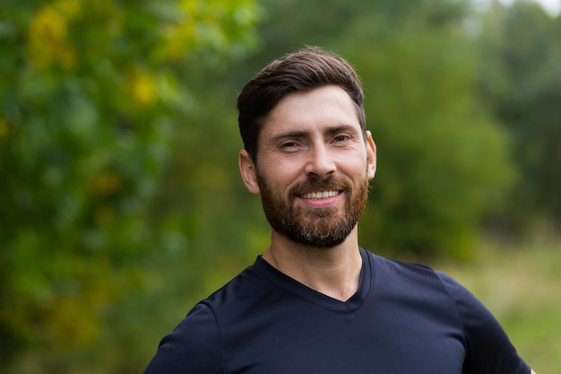 Close up portrait young happy bearded man standing in nature between forest trees relaxes, breathes fresh air closing his eyes. Male enjoys a life of peace calm, quiet in the park. Outdoors. Happiness