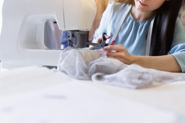 Close-up portrait of young indian seamstress or dressmaker sews on sewing machine in her own workplace. 