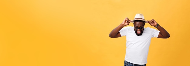 Close up portrait of a young man laughing with hands holding hat isolate over yellow background