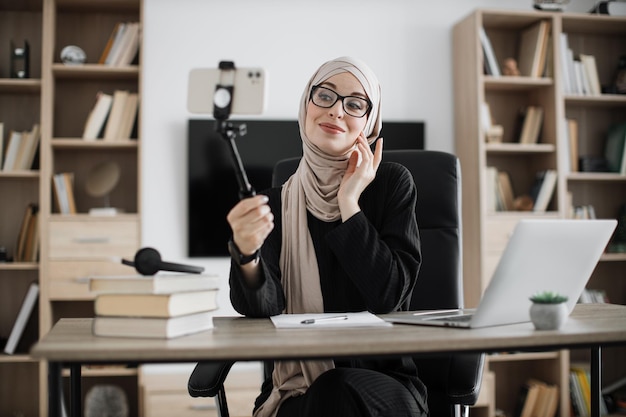 Close up portrait of young muslim woman in hijab taking selfie on her smart phone using stick