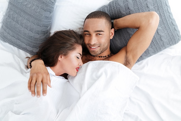 Close-up portrait of a young romantic couple hugging and laying down on a white bed