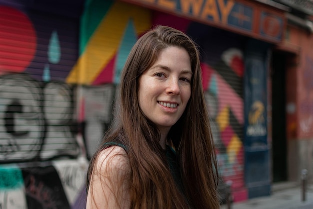 Close-up portrait of young smiling woman knitted hat posing against wall painted with graffiti.