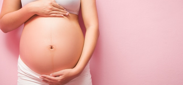 Close up of pregnant belly on pink background