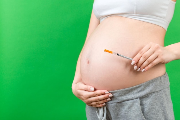 Close up of pregnant woman holding insulin syringe against her belly at colorful background with copy space Diabetes concept