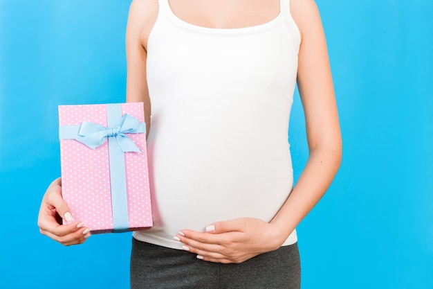 Close up of pregnant woman in home clothing holding pink spotted gift box at blue background Expecting a baby girl Copy space