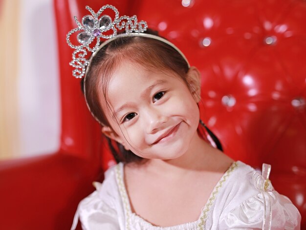 Close-up pretty little girl in beautiful luxurious dress with crown sitting 