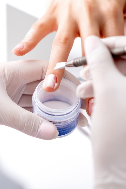 Close up of the process of applying acrylic powder on the nails of a young woman in a beauty salon