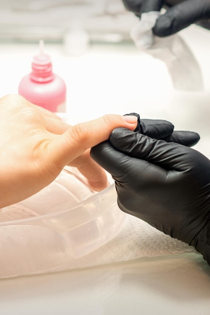 Photo close up professional manicure master holds the female hand of the customer and disinfects nails in a nail salon