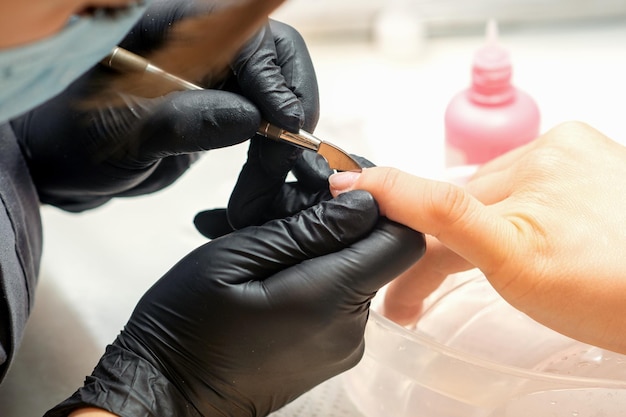 Close up professional manicurist master holding customer hand while using a cuticle pusher in a nail salon