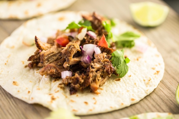 Close up of pulled pork carnitas with pico de gallo on a flour tortilla.