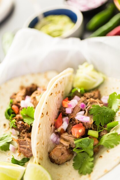 Close up of pulled pork carnitas with pico de gallo on a flour tortilla.