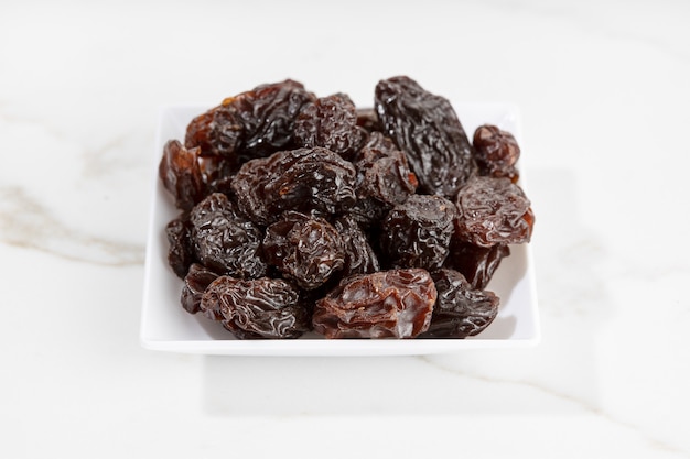 Close up of Raisins on plate isolated on White marble surface. Dried grape