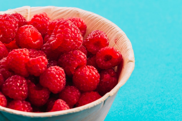 Close-up of raspberries in the bowl on the turquoise backdrop