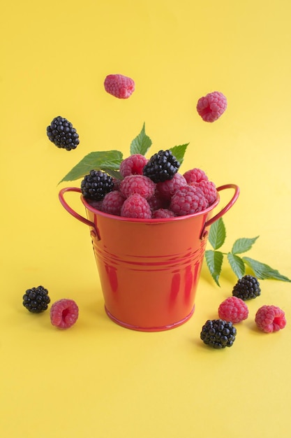 Close-up on raspberry and blackberry in the red bucket on the yellow  background