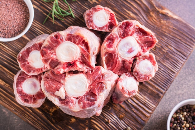 Close up of raw sliced oxtail spices and rosemary on a wooden board top view