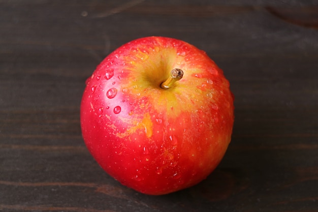 Close up red apple with water droplets isolated on dark brown wooden table