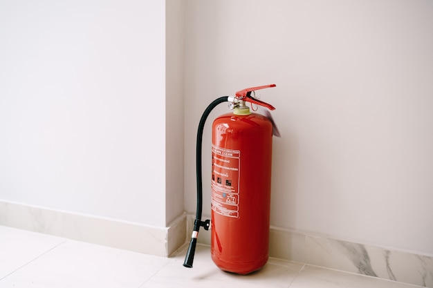 A close-up of a red fire extinguisher on the floor in the corner against a white wall