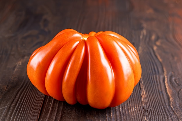 Close up of an red ripe tomato on a wooden board. Funny, weird vegetable. Ugly food.