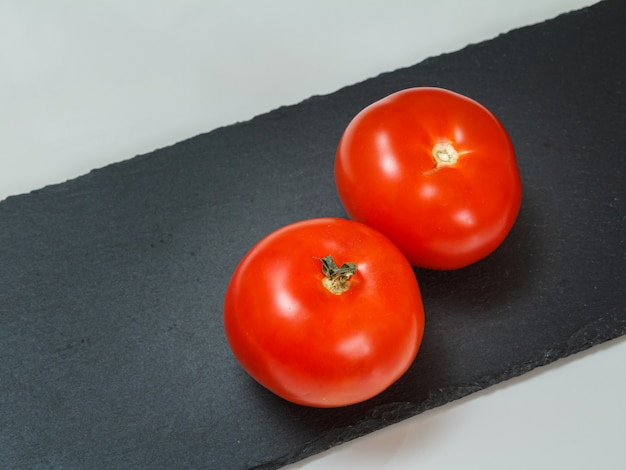 Close-up red ripe tomatoes on the black stone cutting board