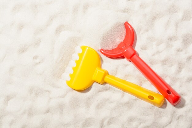 Close-up of red shovel and yellow rake on sand.