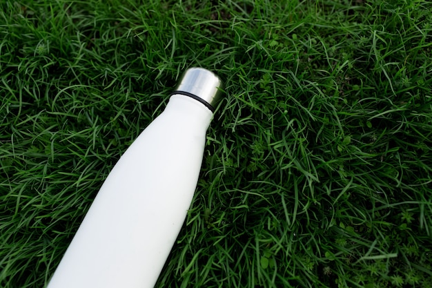 Close-up of reusable, eco steel thermo water bottle of white color on green grass.