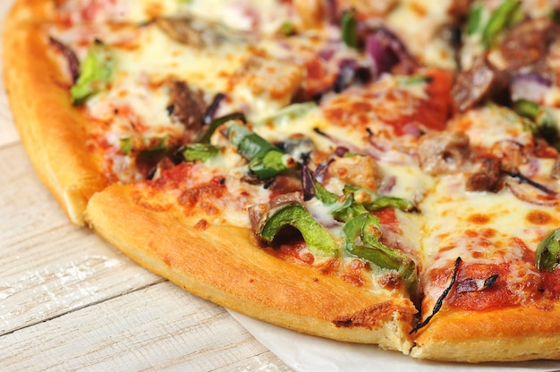 Close up round pizza cut into pieces on a wooden background