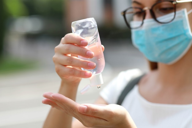 Close up of school girl with medical mask using hand sanitizer gel in city street. Antiseptic, Hygiene and Healthcare concept. Focus on hands.