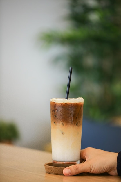 Close up and selective focus hand holding glass of ice caramel macchiato on wooden table.