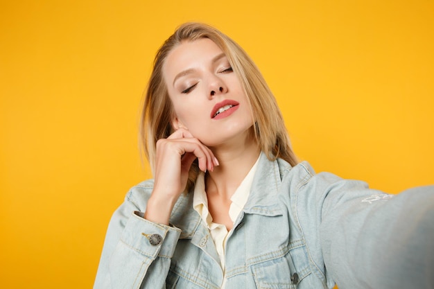 Photo close up selfie shot of tender young woman in denim casual clothes put hand prop up on chin, keeping eyes closed isolated on yellow orange background. people lifestyle concept. mock up copy space.